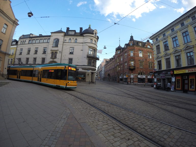 Eine gelbe Straßenbahn fährt durch die kopftsteingepflasterte Altstadt Norrköpings.