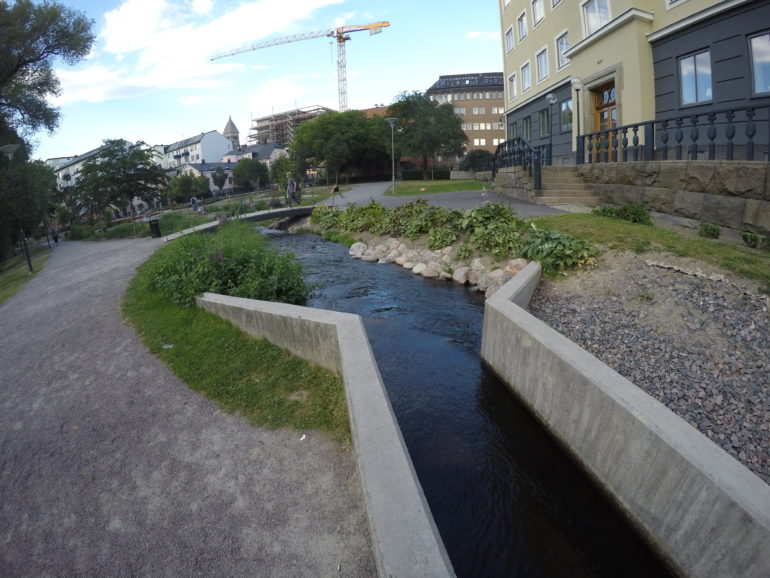 Ein in Betonmauern umfasster kleiner Bach fließt entlang eines Gehweges in Norrköping, Östergötland.