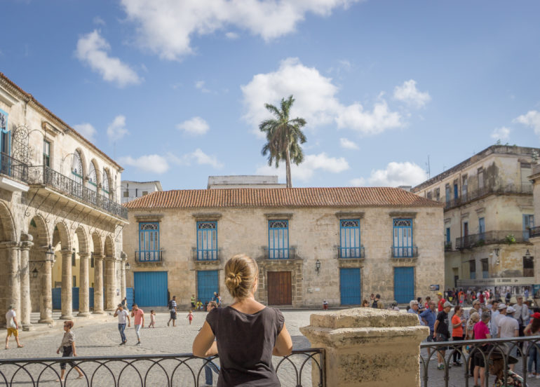 Eine Frau blickt mit dem Rücken zur Kamera auf eine Häuserfassade in der Innenstadt von La Habana in Kuba.