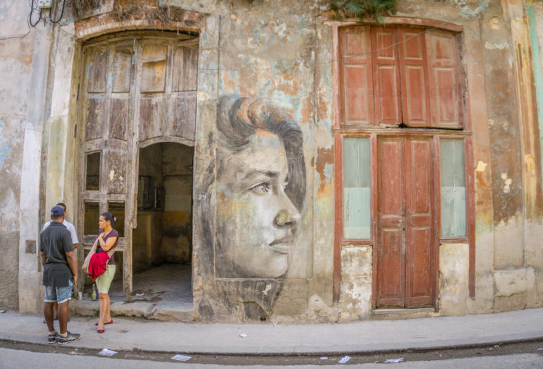 Auf einer Häuserfassade in einer Gasse Havannas ist das Portrait einer attraktiven Frau abgebildet.