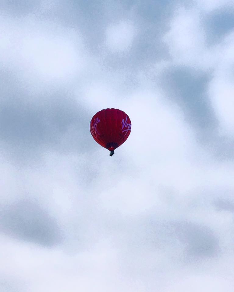 Ein roter Heißluftballon steigt zum Balloon-Fiesta in den bewölkten Himmel von Bristol, England.