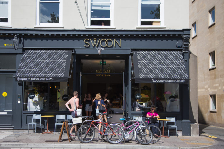Menschen begeben sich Richtung Eingang des Café Swoon Gelato in Bristol mit seiner dunklen Hausfassade, seinen schwarzen Markisen und dem goldenen Schriftzug.