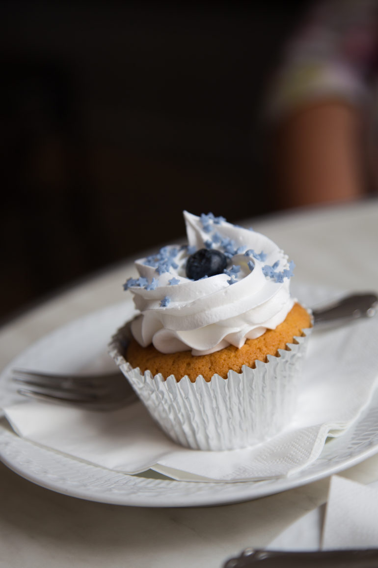 Auf einem Teller wird ein Cupcake mit weißer Creme, blauer Zuckersternchen und Blaubeere in Kopenhagen im Serenity Cupcakes serviert.