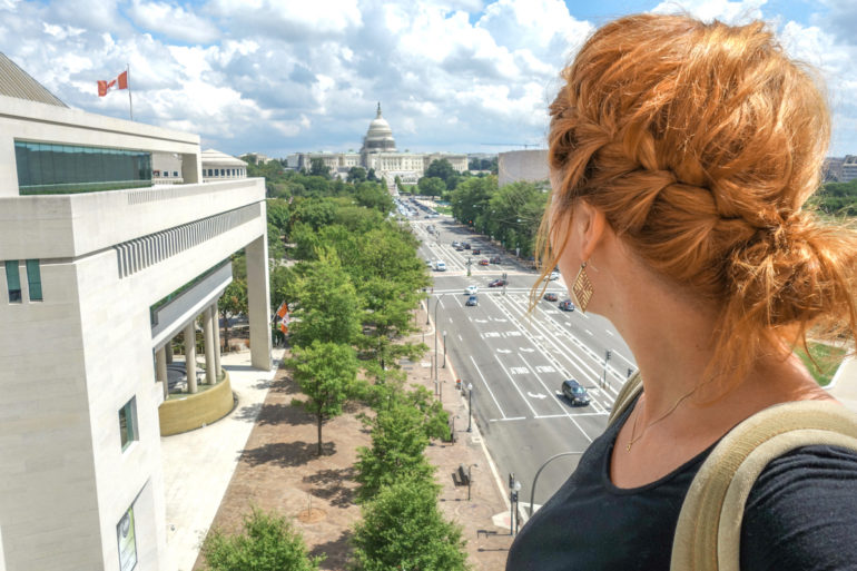 Auf der Dachterasse des Newseums in Washington D.C. wirft die Bloggerin mit ihren roten, gepflochtenen Haaren den Blick nach Vorne gerichtet auf die Straße und das US Capitol.