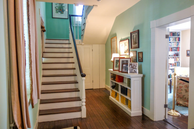 Im mintfarbenen Eingangsbereich des Marshall House in Virginia führt eine weiße Holztreppe in die obere Etage, im Sideboard gegenüber befinden sich zahlreiche Bilder der Familie Marshall.