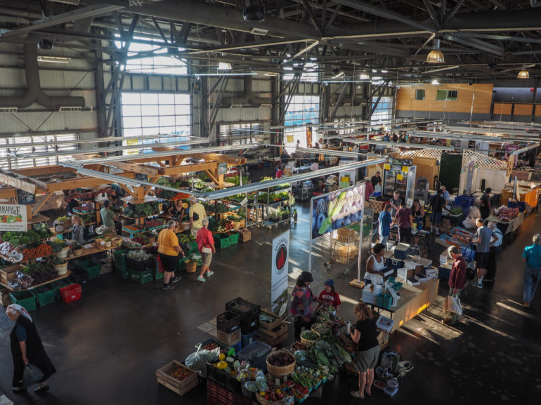 In dem ältesten kanadischen Bauernmarkt "Seaport Farmers Market" in Nova Scotia kaufen Menschen in einer großen Markthalle an Holzständen frische Lebensmittel.