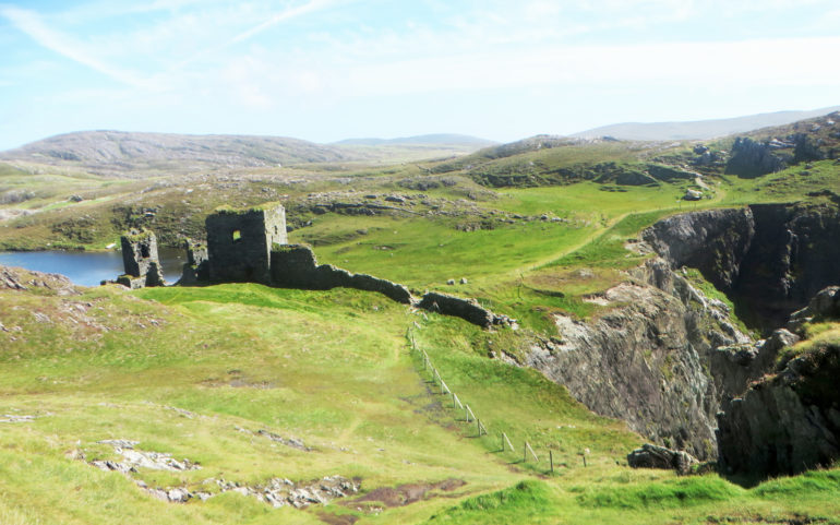 Die Ruine der Burg Three Castle Head inmitten der irischen Landschaft.