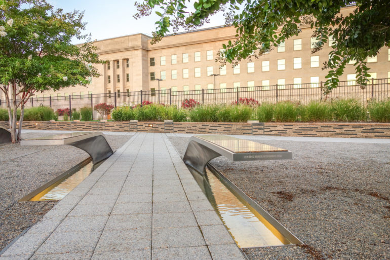 Das Pentagon Memorial vor dem Pentagon Gebäude in Virginia besteht aus einem länglichen Weg aus Steinplatten, die links und rechts von Metall in Flügelform gefasst sind.
