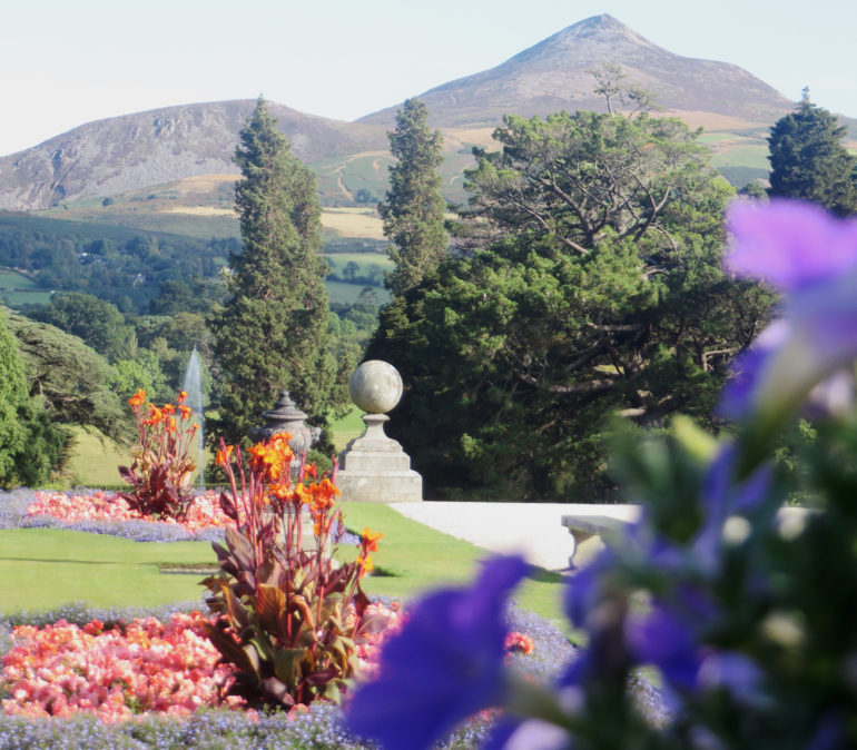An den Blumen und Bäumen des Powerscourt Gardens in Irland vorbeigezoomt ergibt sich der Blick auf die umliegenden Hügel.