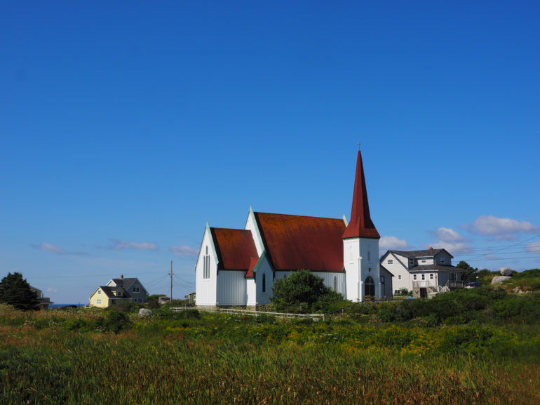 Hinter einer Wiese steht die weiße St. John's Aglican Church aus Holz und mit roten Dächern.