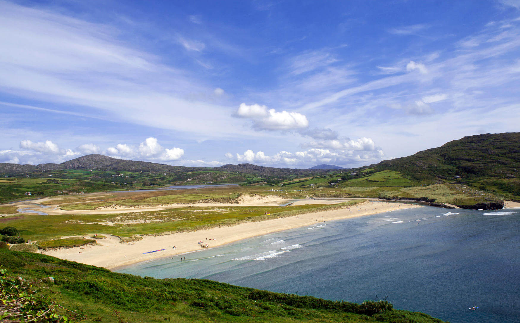 Inmitten grüner Hügeln fließt das Meer an den Sandstrand der Halbinsel Mizen im Süden Irlands.