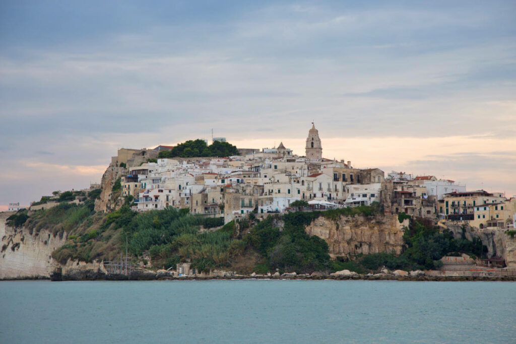 Vom Meer aus blickt man auf das Dorf Vieste in Apulien, das auf der Halbinsel Gargano im Abendlicht liegt.