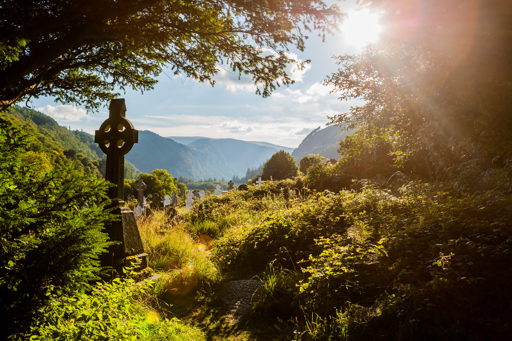 Über alten Grabmälern inmitten der grünen irischen Hügeln scheint die Sonne durch.