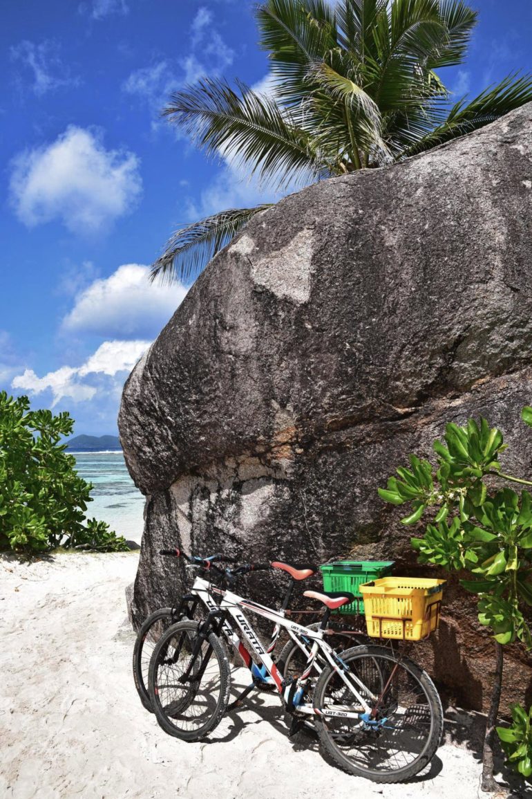 Am Strand La Digue lehnen zwei Fahrräder mit Körbchen an einer Felswand.