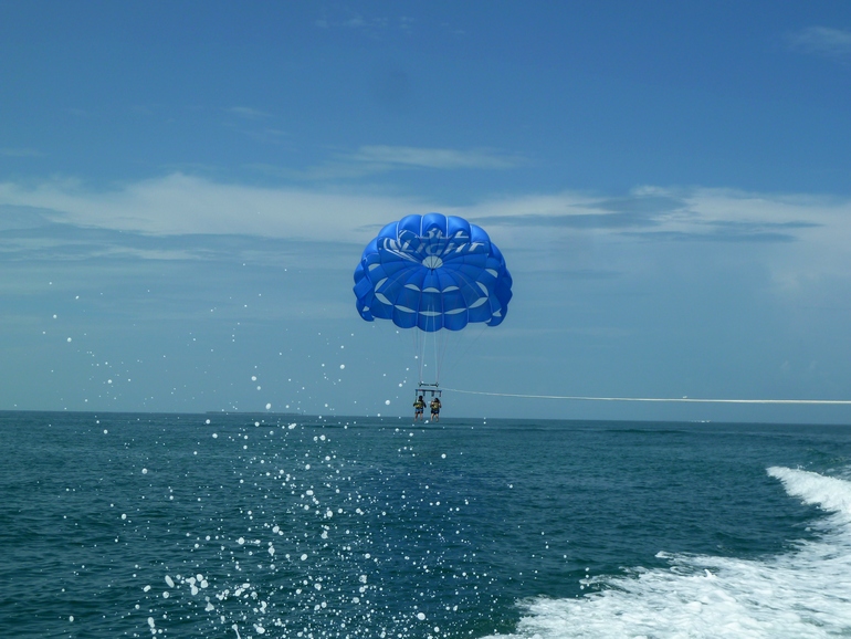 Zwei Personen an einem blauen Paraglidingschirm steigen über das glitzernde Meer von Key West in die Lüfte.