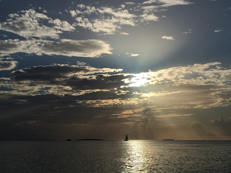 Ein einsames Segelboot schippert auf dem Meer vor Key West, während sich die untergehende Sonne hinter den Wolken versteckt.