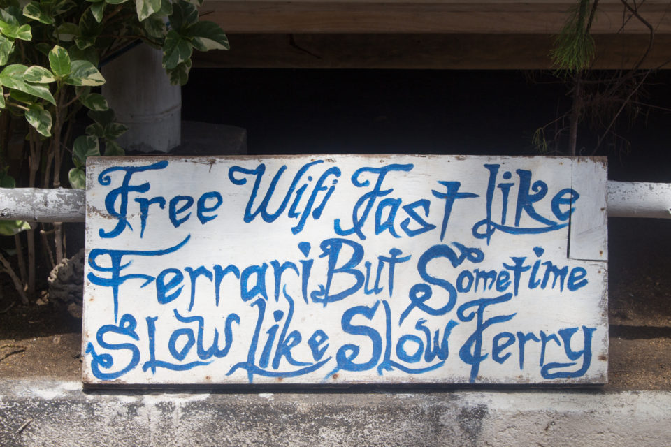 Ein weißes Holzschild mit blauer Schnörkelschrift nahe einer Tauchschule auf den Gili Insel Gili Air gibt Auskunft über den Wifi Zugang.