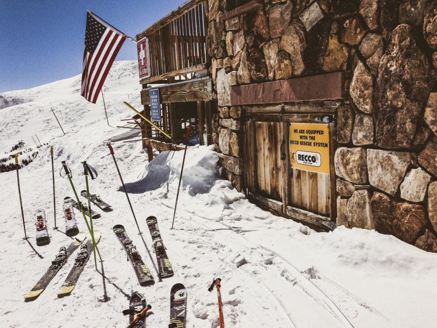 Einige Ski und Skistöcke wurden in den Schnee vor der Stein-Holzhütte mit amerikanischer und Schweizer Flagge gesteckt, die auf der Piste in Breckenridge, USA steht.