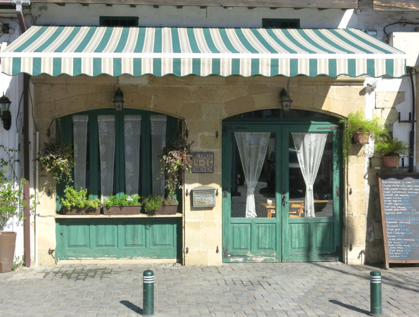 Auf einer Seitenstraße in Larnaka, Zypern, befindet sich ein Dorfladen, die Fenster und Türen sind in grün gehalten und mit Pflanzen geschmückt und die Markise in grün-weiß schützt vor der Sonne.