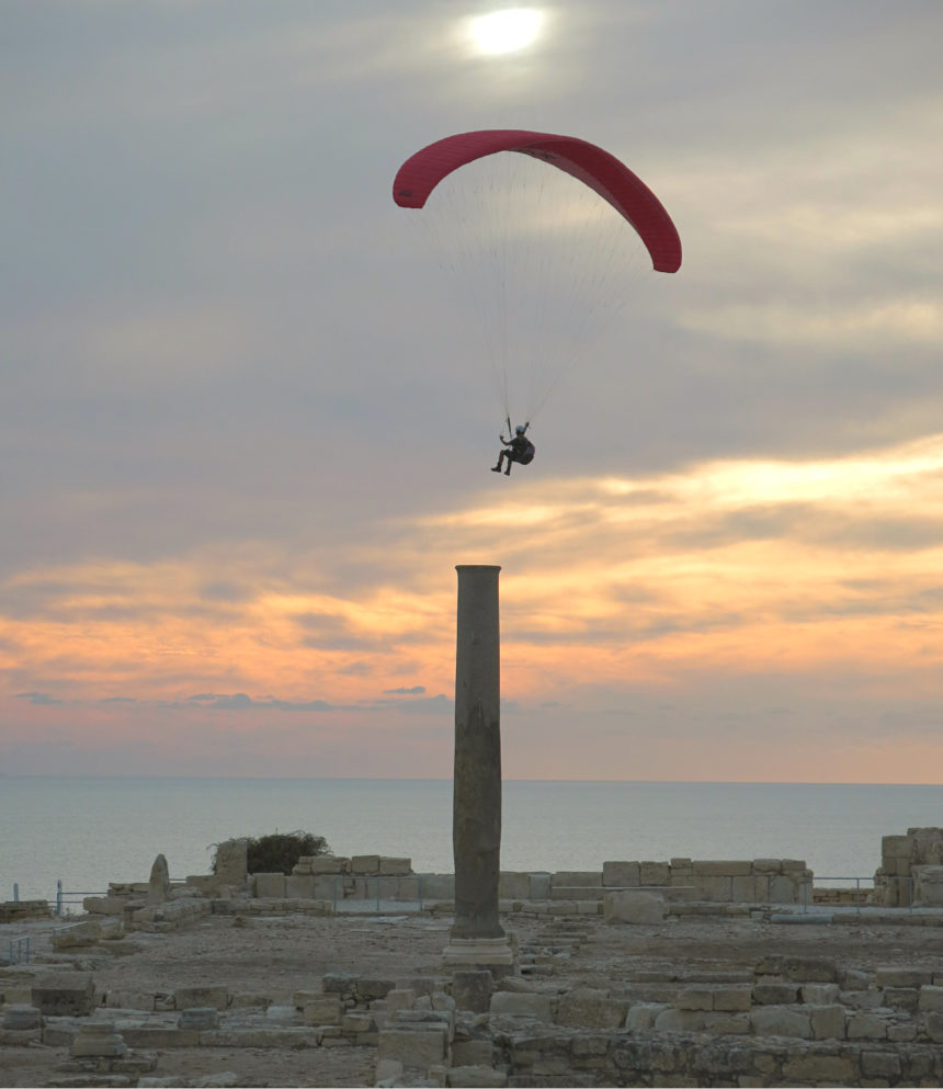 In der zypriotischen Abendsonne segelt ein Gleitschirmflieger über die archäologische Stätte Kourion, das an einer Anhöhe vorm Meer liegt.