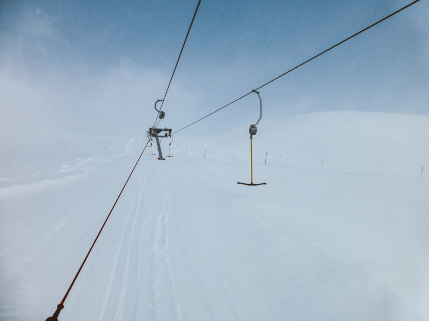 Auf einer stark beschneiten Piste in Norwegen fährt ein Skilift mit Bügel menschenleer den Hang hinauf.