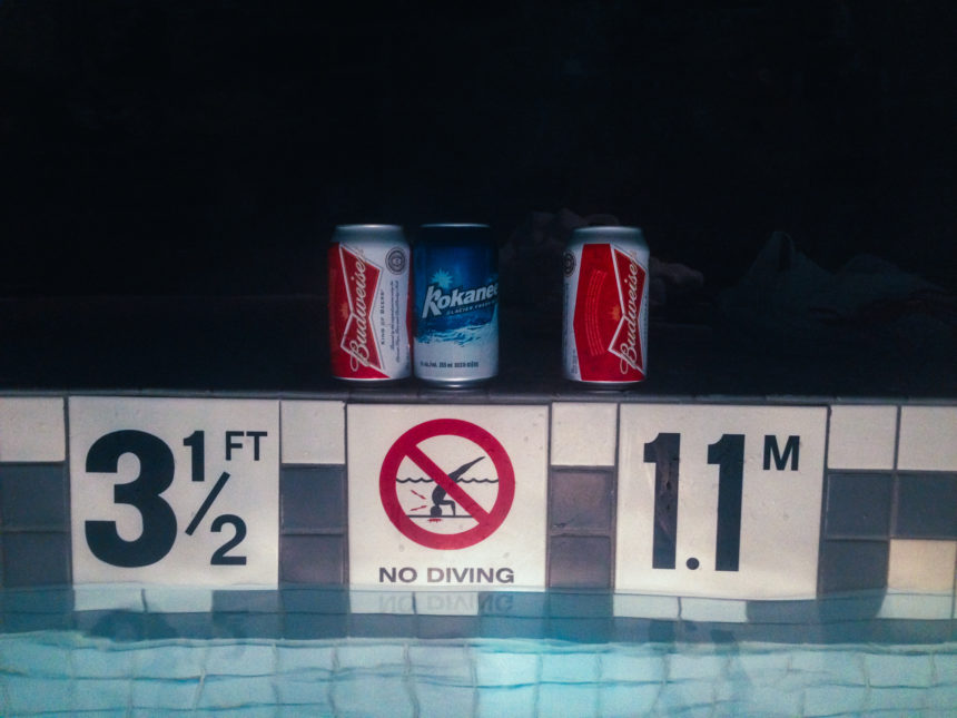 Drei Getränkedosen stehen am Rand eines Pools und seinen Hinweisschildern.