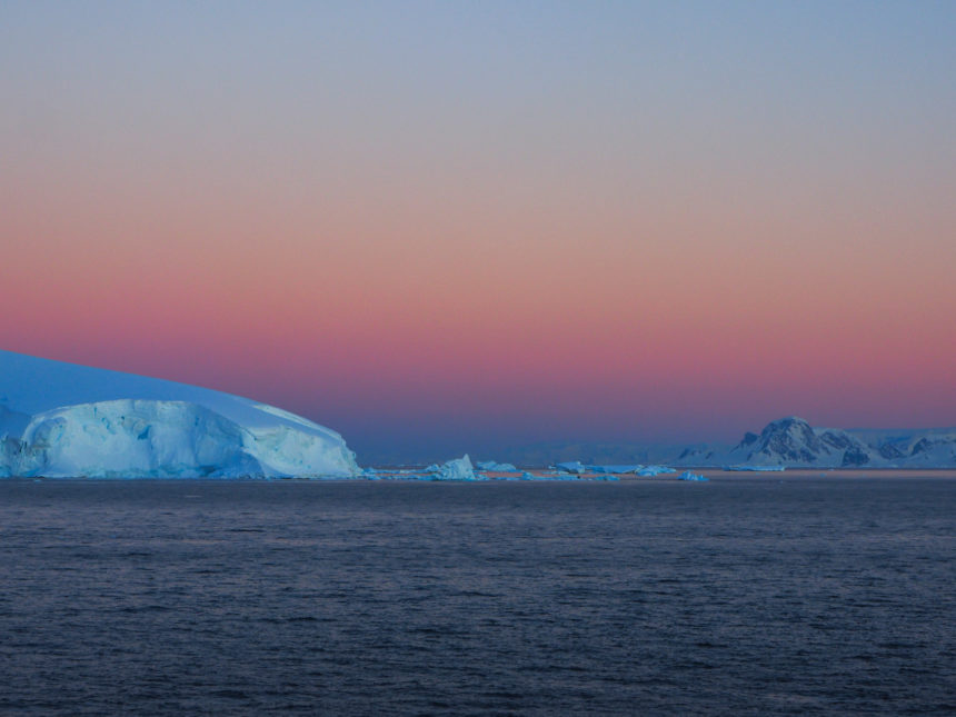 Over the Neumayer Canal and the icebergs, the sky turns pink at sunset.