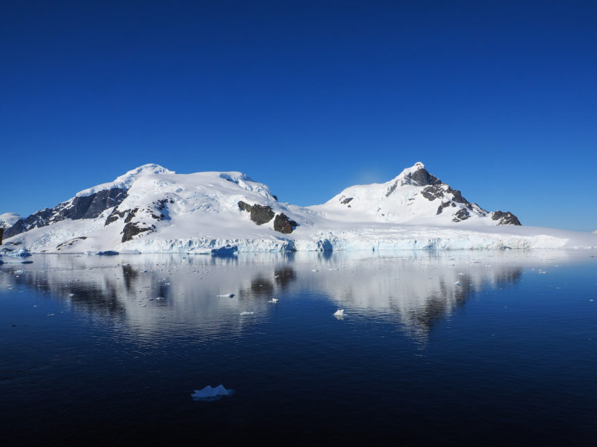 The rocky and snow-capped Cuverville Island is reflected on the crystal clear sea.