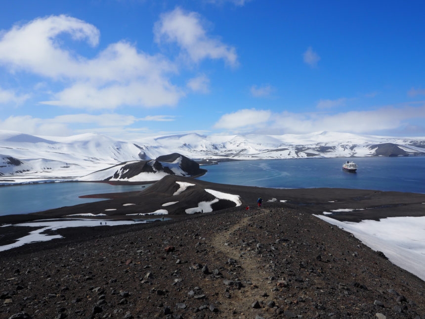 Der Blick über Deception Island, Antarktis zeigt eine schneebedeckte Kraterlandschaften inmitten des Meeres.