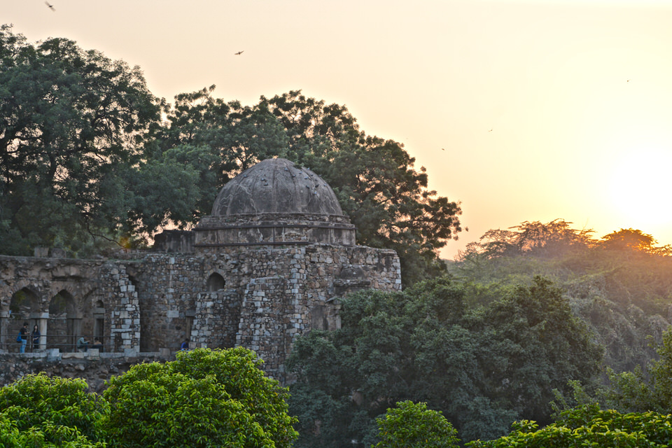 Hinter dem mittelalterlichen Monument der Hauz Khas und großen Bäumen in Delhi, Indien geht die Sonne unter.