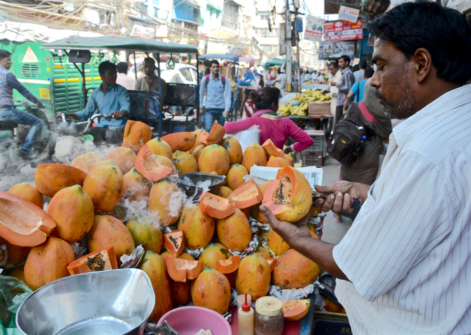 Auf dem Chowri Bazar in Old Delhi schneidet ein Händler an seinem Stand eine frische Papaya auf.