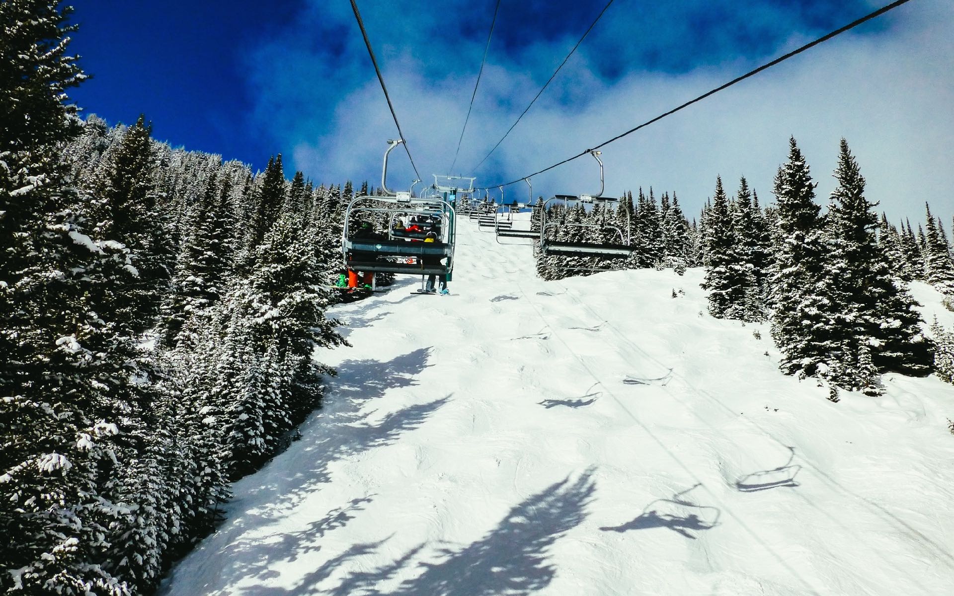 Ein Sessellift in Kanada fährt bei strahlend blauem Himmel die Skifahrer den schneebedeckten Hang hinauf.
