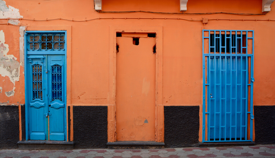 Auf den Kapverden in Sao Vicente Mindelo sind die Fassaden der Häuser in bunten und kräftigen Farben getaucht, auf diesem Bild umrahmt die knallig orange Wand zwei blaue Türen.