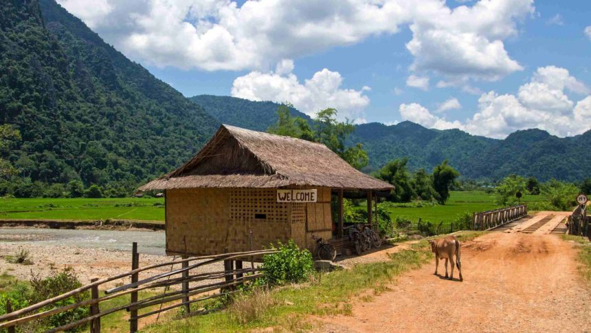 Auf den sandigen Straßen der Umgebung von Vang Vieng bei Laos erwartet einem grünbewachsenes Bergpanorama, kleine Strohhütten und ab und an Kühe, die den Weg kreuzen.