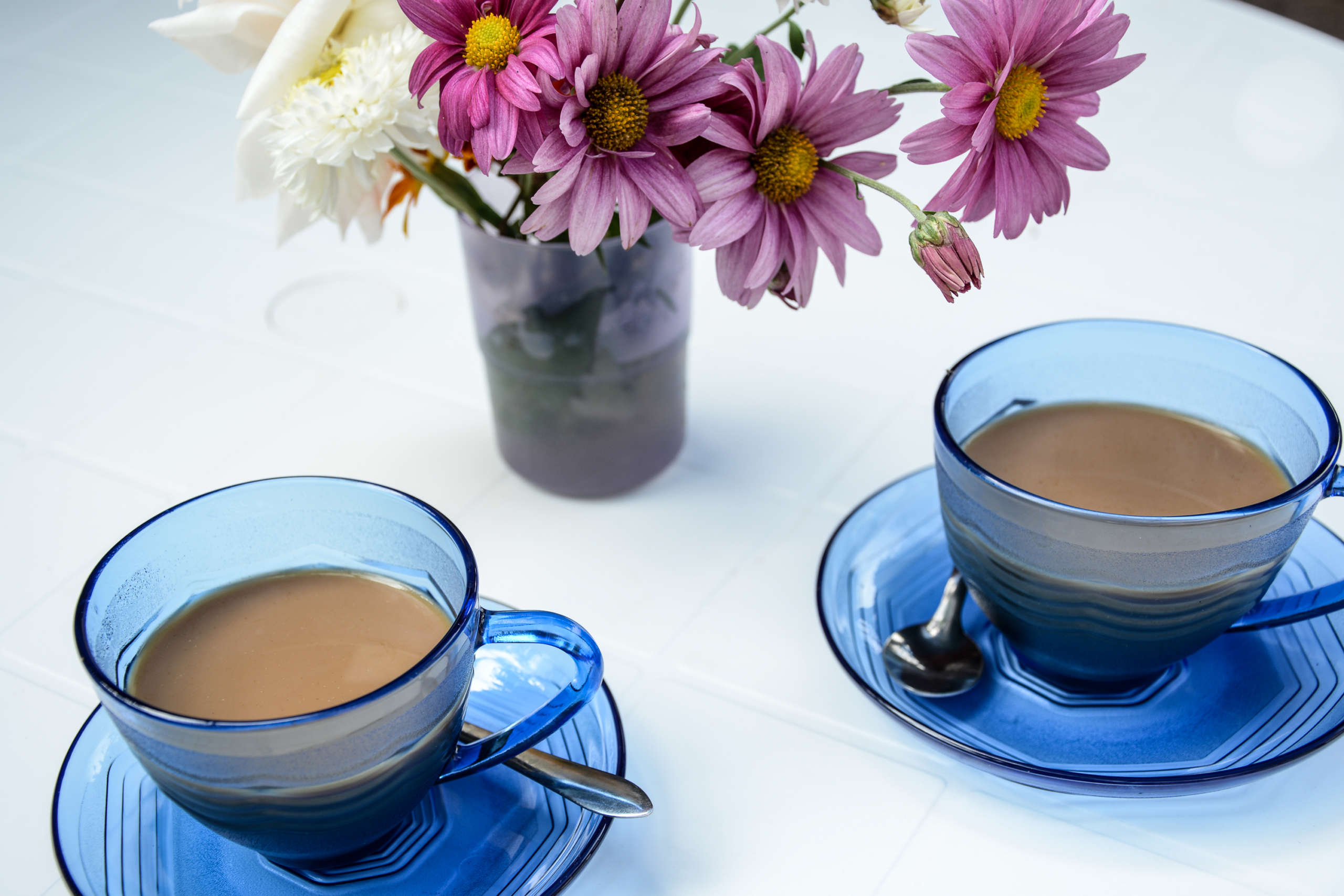 Zwei Kaffeetassen auf einem Tisch, dahinter Blumen in der Vase.