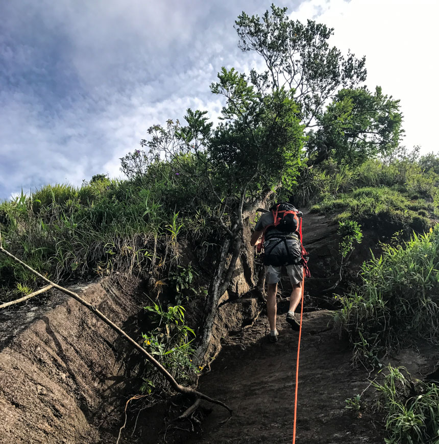 Der Aufstieg eines Wanderers bei Pedra da Gavea ist steil und führt über einen erdigen Weg entlang eines roten Seils.