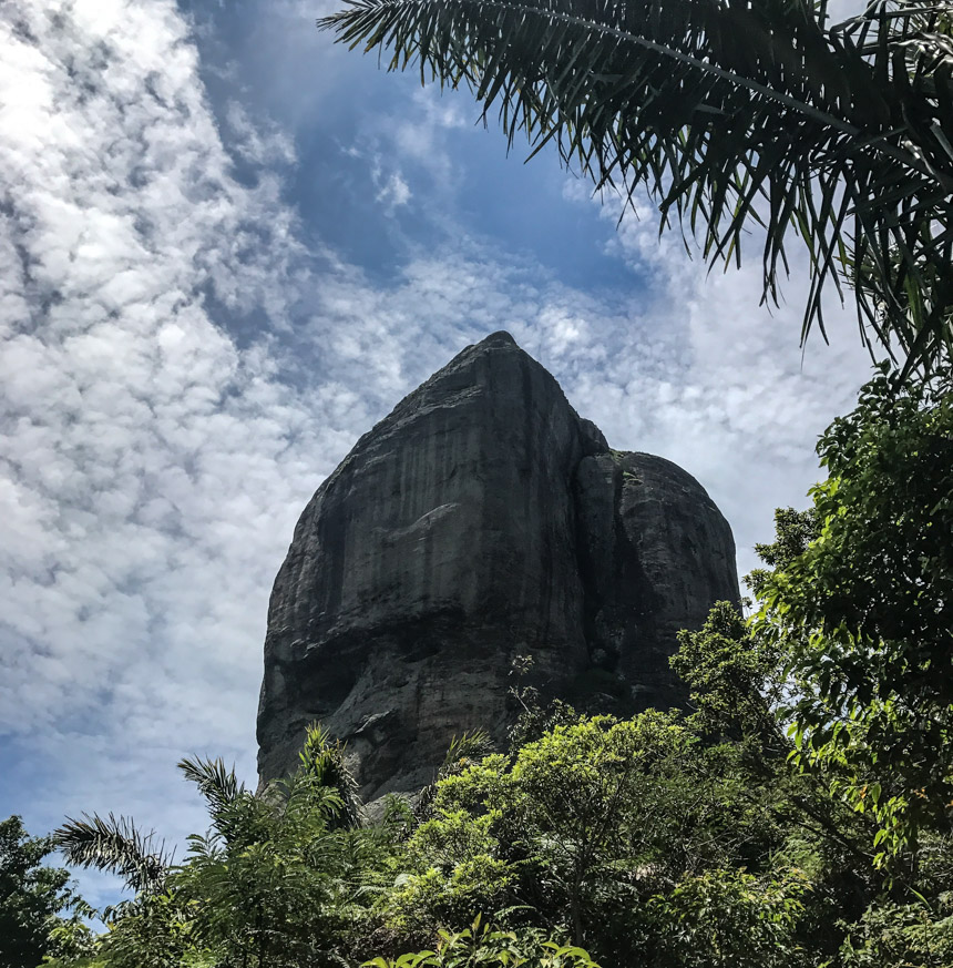 Der steile Berg Pedra da Gavea in Rio de Janeiro ragt zwischen grüner Natur in den Himmel.