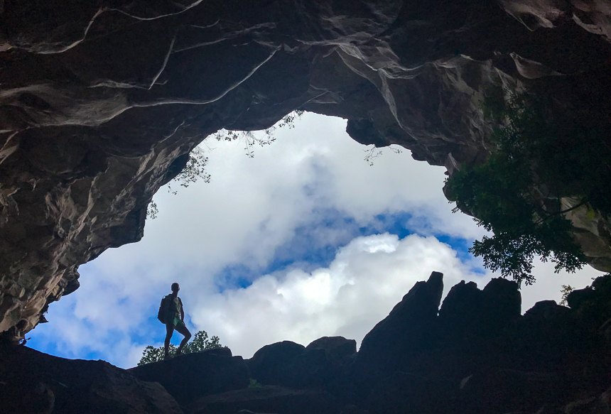 Im Schatten eines Höhleneingang in Chapada Diamantina steht eine Wanderin, hinter ihr der wolkenbehangende Himmel.