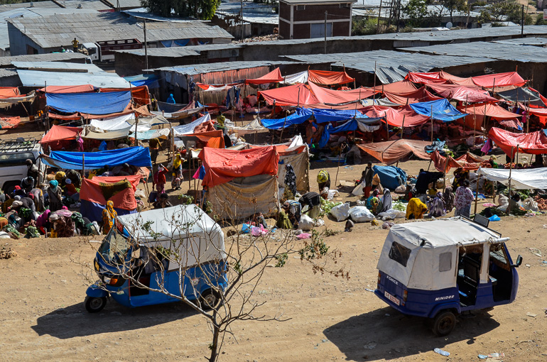 Auf einem Gewürzmarkt in Harar, Äthiopien schützen rote und blaue Planen die Stände vor der Sonne, zwei kleine Lieferwagen kreuzen den Weg.