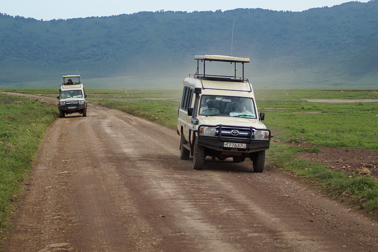 Zwei weiße Land Cruiser fahren entlang einer Schotterstraße in Tansania