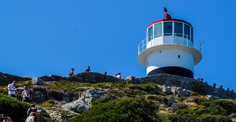 Touristen besteigen den grünbewachsenen Berg hoch zum Leuchtturm in Südafrikas Kapregion - Kap der guten Hoffnung.