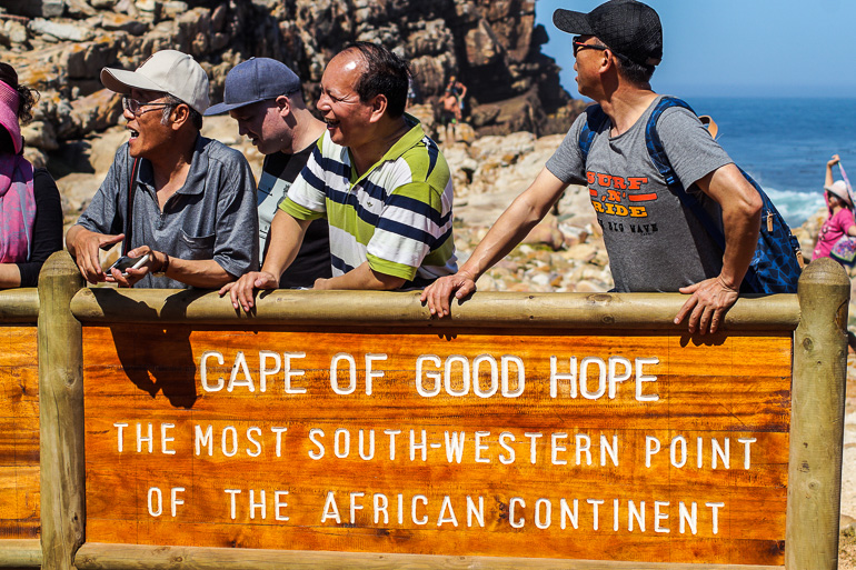Asiatische Touristen posieren vor einem Schild, das den südwestlichsten Teil Afrikas markiert in Südafrikas Kapregion - Kap der guten Hoffnung.