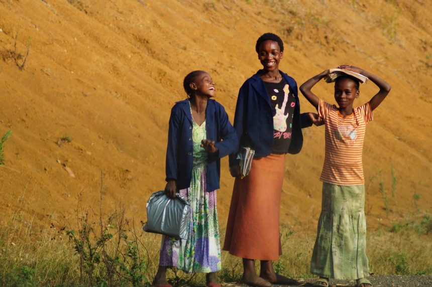 Drei einheimische Mädchen lachen auf einem Feld in Kafa, Äthiopien, in die Kamera, in ihren Händen tragen sie Hefte und Bücher.