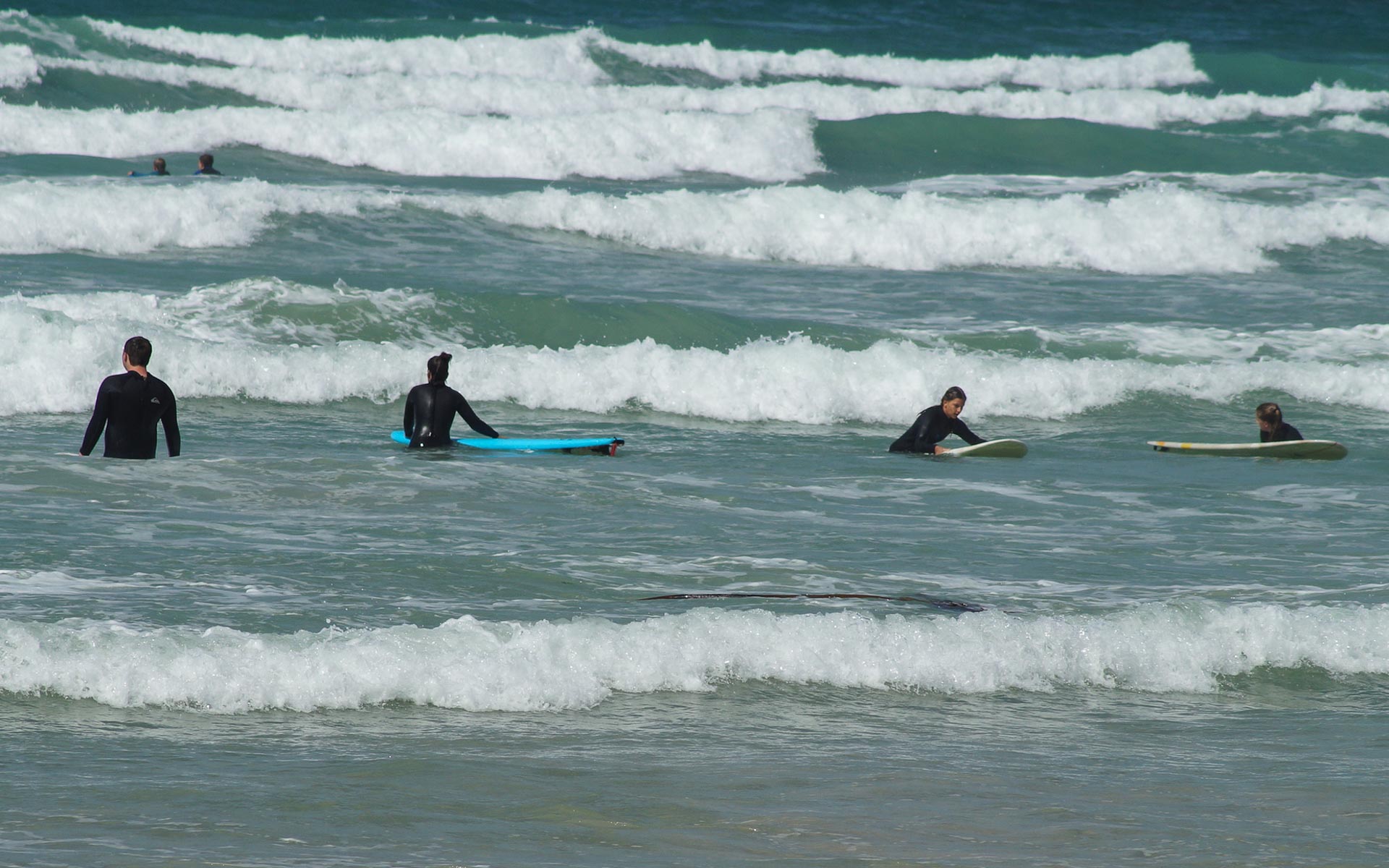 In der Südafrikanischen Kapregion Muizenberg Beach warten vier Surfer im Meer auf eine Welle.