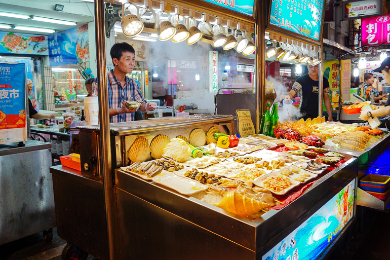 In Kaoshiung, Taiwan befindet sich der Liuhe Nachtmarkt, bei dem Händler in ihren beleuchteten Buden frische Lebensmittel anbieten.