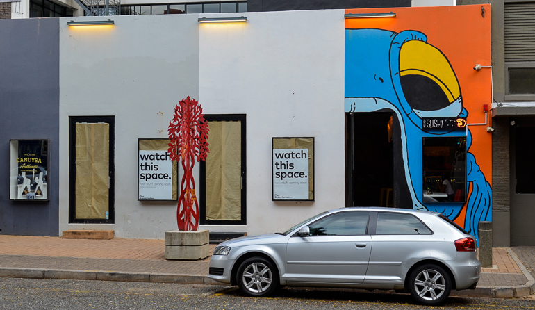 Ein silbernes Auto steht in Johannesburg vor einem Sushi-Restaurant dessen Eingang und Hauswand mit einem riesigen Fischmaul bemalt wurde.