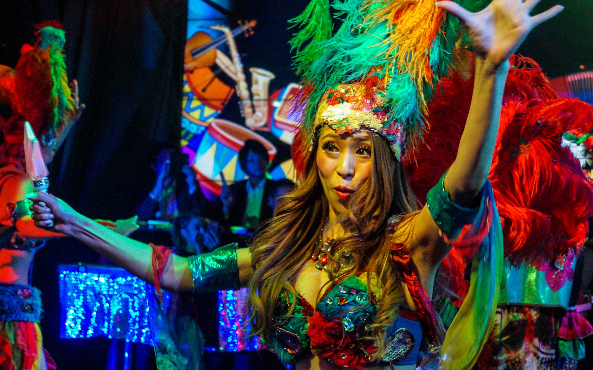 Eine bunt gekleidete Frau mit einem riesigen Federnkopfschmuck tanzt in dem Robot Restaurant in Tokio, Japan.