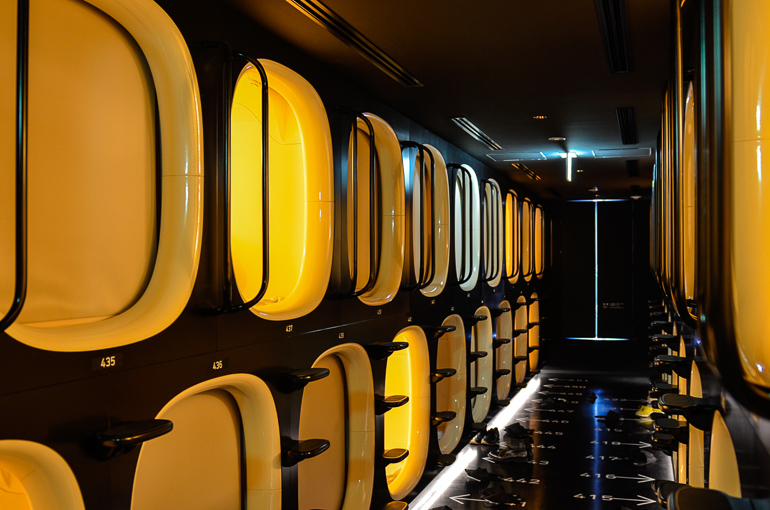 Ein Blick in Tokios Kapselhotel zeigt einen dunklen schwarzen Flur mit vielen gelb beleuchteten Eingängen zu den Schlafkapseln.