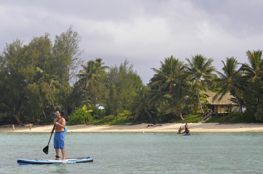 Am Strand der Lagune Rarotongas paddelt ein Stand-Up-Paddler im ruhigen Gewässer.