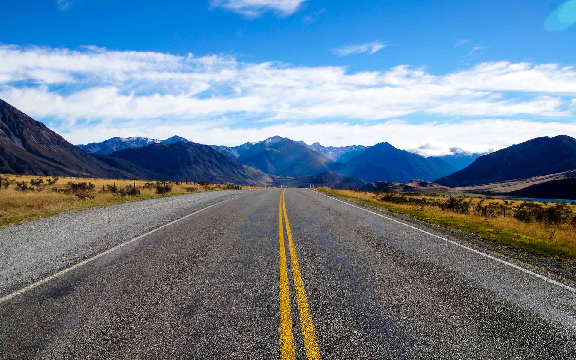 Eine leere Straße in Neuseeland führt geradeaus in das Bergpanorama.